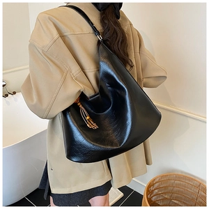 Detail of black glossy pleated tote bag with wooden bead tassel on a model's shoulder