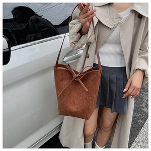 Detail of a brown suede bucket bag with a bow accent, worn by a model in casual attire