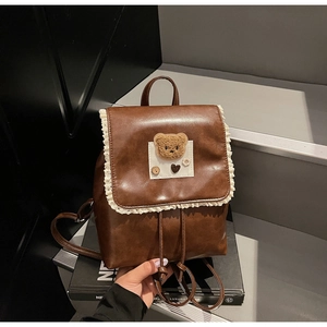 Detail of dark brown leather backpack featuring white lace trim and a cute plush bear patch