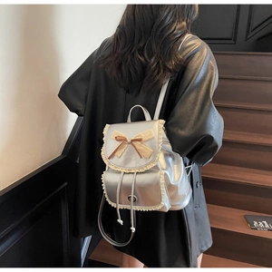 Detail of silver metallic backpack with lace trim and bow on a model against stairs