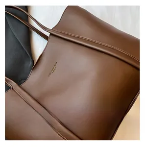 Dettaglio ravvicinato della borsa tote in pelle marrone con logo dorato e cuciture fini