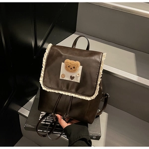 Detail of dark brown leather backpack with lace trim and plush bear embroidery