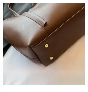 Dettaglio del fondo della borsa tote in pelle marrone con cuciture e borchie dorate