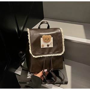 Detailed view of lace trim and plush bear patch on dark brown leather backpack