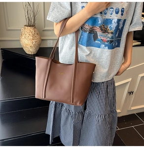 Dettaglio di una borsa tote strutturata in pelle marrone scuro opaca con outfit casual