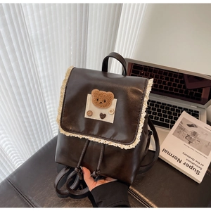 Close-up of brown leather backpack with lace trim, plush bear patch and heart ornaments