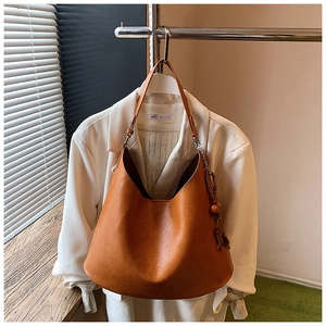 Detail of caramel brown Hobo shoulder bag with natural leather texture and wooden bead charm