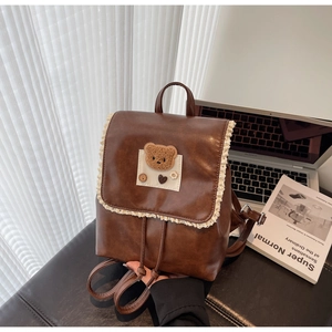 Detail of vintage brown leather backpack with cream lace trim and plush bear decoration
