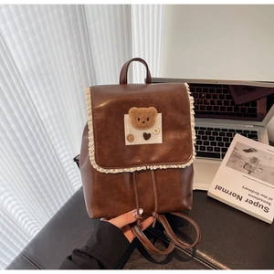 Detail of vintage brown leather backpack with lace trim and plush bear on a desk
