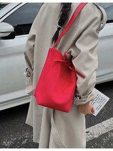 Minimalist red suede bucket shoulder bag with tie detail worn over a beige trench coat