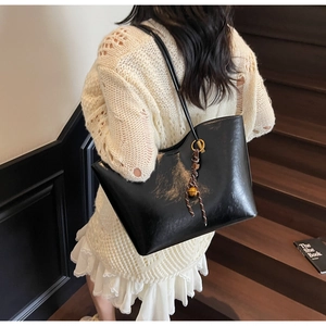 Detailansicht der schwarzen Lackleder-Tote-Bag mit Glockenanhänger an einem Model