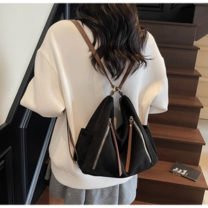 Detail of black suede backpack with double zippers, tassels and brown leather straps