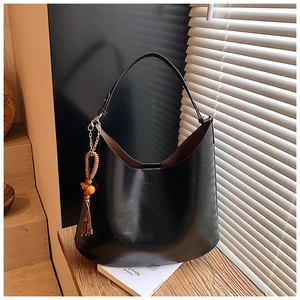 Detail of black faux leather bucket bag with metal hook and beaded tassel charm