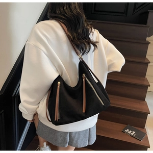 Detailed view of black hobo bag with brown leather straps and golden zippers shown on a model