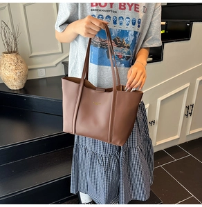 Dettaglio di una borsa tote in pelle marrone con spalline sottili e logo dorato raffinato