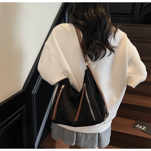 Detail of black matte shoulder bag featuring brown leather straps and long zipper pulls