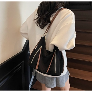 Detail view of large black retro tote bag with brown leather straps on a wooden staircase