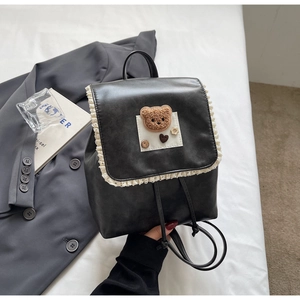 Close-up of black PU leather backpack with white lace trim and cute plush bear patch