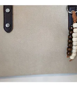 Detail of beige textured fabric tote with brown leather strap and wooden bead charm