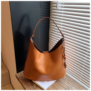 Detail of caramel leather tote bag with wooden bead tassel charm on wooden table