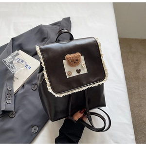 Detail of vintage brown leather backpack featuring lace edges and plush bear emblem
