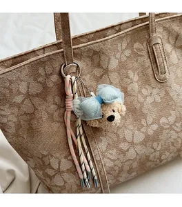 Detail eines Plüsch-Hundeanhängers mit blauer Spitzenschleife an der Handtasche