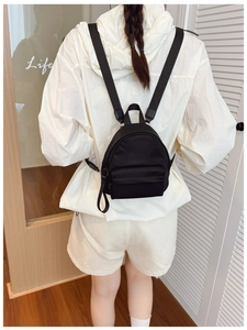 Back view of a mini black nylon backpack on a model in a cozy home setting