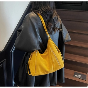 Detailed texture of ginger yellow suede hobo bag with fringe zippers on a black coat