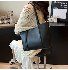Dettaglio di una grande borsa tote in pelle nera con logo dorato su una modella al caffè