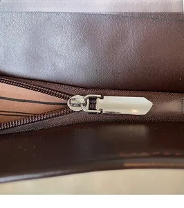 Close-up of smooth silver metal zipper and striped lining on dark brown tote bag