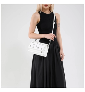 Close-up of white baguette bag with silver metal eyelets and leather shoulder strap
