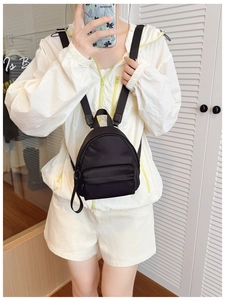 Detail view of a lightweight black nylon mini backpack with adjustable straps on a model