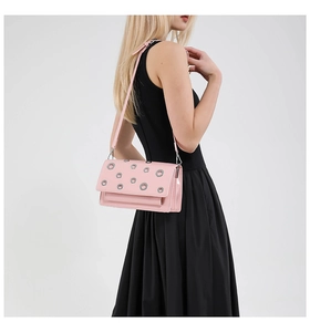 Detail of pink faux leather crossbody bag with silver eyelets worn on black dress