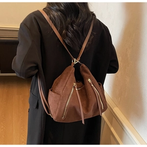 Brown suede backpack with gold zipper detail worn by a model in a black winter coat
