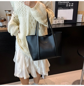 Dettaglio di una borsa tote in pelle nera con logo dorato in un ambiente da caffè