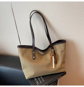 Detail of olive canvas tote bag featuring brown leather trim and wooden bead ornament