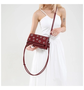 Detail of burgundy crossbody bag with silver grommets worn over a white dress