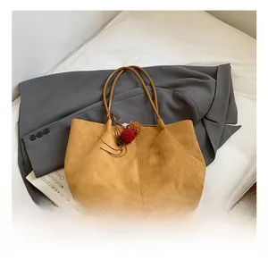 Detail of ginger tote bag with vertical stitching and decorative fur ball on grey blazer