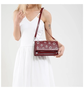 Deep red leather crossbody bag with silver eyelet accents shown on a model