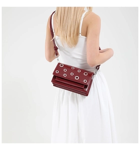 Detail of dark red crossbody bag with silver eyelet rivets worn by a model in studio