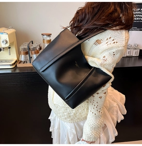 Dettaglio della borsa tote in pelle nera con logo dorato in un ambiente caldo di caffè
