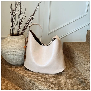 Close-up of cream leather hobo bag with wood bead charm on a minimalist textured background