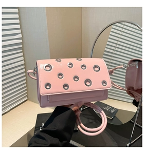 Detailed close-up of pink synthetic leather crossbody bag with silver metal eyelets