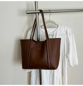 Dettaglio di una grande borsa tote marrone scuro con logo dorato su un appendino