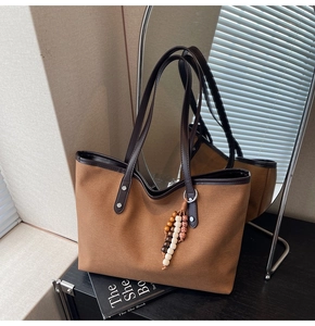 Detail of a brown canvas tote bag with leather straps and a beaded tassel accessory