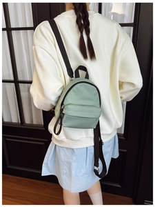Rear view of a mint green mini nylon backpack worn by a model against a dark door