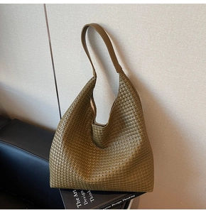 Close-up of olive green woven tote bag with smooth leather strap against a textured wall