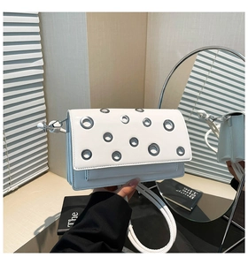 Detail of white square crossbody bag with silver metal grommets shown in mirror reflection
