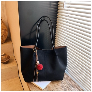 Detail of black suede tote bag with red pompom charm and wooden beads on a wooden ledge