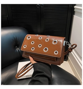 Close-up of brown glossy leather crossbody bag featuring silver grommet decorations